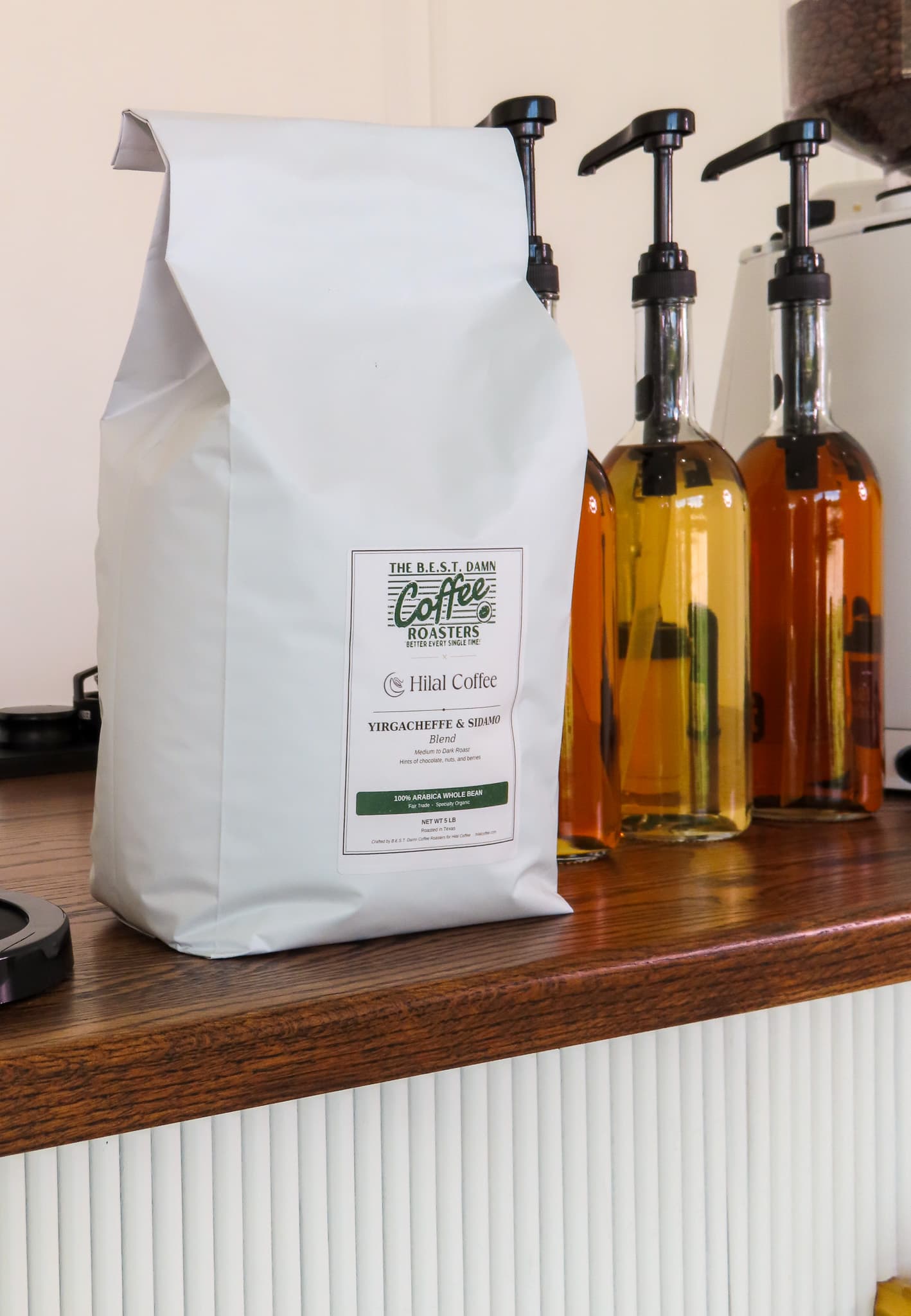 A bag of Hilal Coffee's signature coffee blend beside flavor syrups